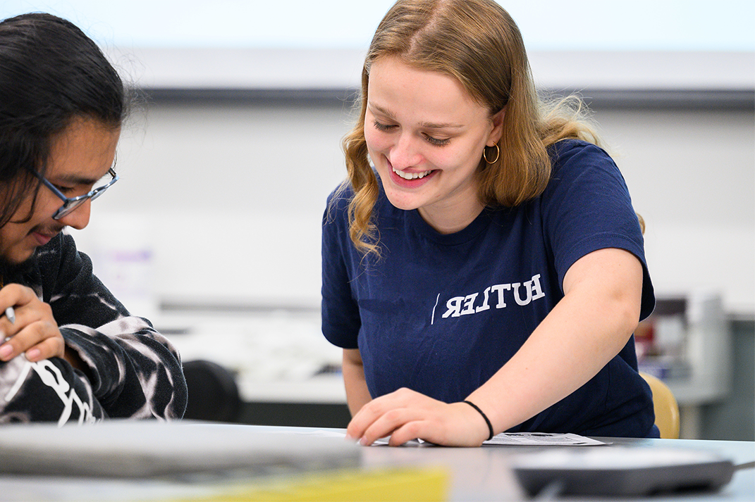 female student in Butler shirt assisting male high school student at table